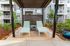 Chic outdoor patio with two sleek lounge chairs under a stylish pergola, surrounded by lush greenery and modern apartment balconies in the background.