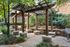 Inviting outdoor patio area with wooden pergola and built-in grill set amidst lush greenery.
