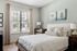 Bright and airy bedroom with soft color scheme, featuring a comfortable bed, decorative pillows, elegant curtains, and nature-inspired artwork.