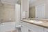 Modern bathroom featuring a sleek countertop, white cabinetry, and a stylish bathtub with marble tile surround.
