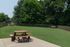 Spacious green lawn with wooden picnic tables and benches, surrounded by lush trees and a protective fence.