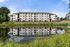 Elegant four-story apartment complex with a reflective lake and lush greenery.