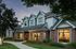 Charming townhouse exterior with brick and pastel siding, featuring large well-lit windows and lush landscaping at sunset.