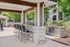 Charming outdoor kitchen and seating area featuring a sleek barbecue grill, spacious bar with stools, and lush green surroundings.