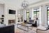 Elegant living room with modern chandelier, plush leather sofas, and a cozy fireplace, featuring large windows offering a bright poolside view.