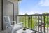 Charming balcony view featuring modern outdoor seating, lush greenery, and a serene residential backdrop under a clear blue sky.