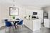 Bright and modern kitchen dining area featuring elegant white cabinets, a sleek marble countertop, stylish blue velvet chairs, and contemporary decor.
