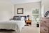 Bright and inviting bedroom with a stylish gray upholstered bed, natural light streaming through large windows, modern decor, and a cozy atmosphere.