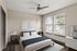 Bright and modern bedroom with a large bed, sleek ceiling fan, and natural light streaming through two large windows.