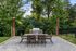 Inviting outdoor patio with dining set, grill, and string lights under lush greenery.