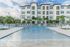 Elegant apartment complex with a shimmering pool surrounded by lush palm trees and seating areas.