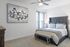 Tasteful bedroom with a plush grey bed, modern artwork on the wall, and soft natural lighting.