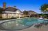 Inviting evening view of a luxurious apartment complex with a sparkling swimming pool surrounded by lush greenery and elegant architecture.