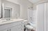 Modern bathroom with sleek vanity, large mirror, and a pristine bathtub surrounded by elegant white tiles.