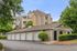 Charming apartment complex with modern architecture and individual garages, surrounded by lush greenery and a well-maintained driveway.