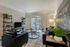 Model apartment living room with gray hardwood style flooring and dark gray furniture including a couch, armchair, coffee table, side table, and entertainment stand