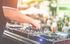 Stock photo of a DJ using a mixing board. The photo has a colorful filter and there is a crowd in the background.