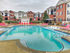 The pool area at our apartments in Tuscaloosa, featuring red pool chairs, umbrellas, and a clubhouse.