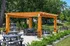 Charming outdoor seating area with wooden pergola and modern picnic tables amidst lush greenery.