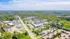 Aerial view of a vibrant suburban neighborhood showcasing modern apartment complexes, lush green spaces, and bustling commercial areas under a bright blue sky.