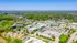 Aerial view of a vibrant community surrounded by lush green forests and featuring modern residential buildings, commercial spaces, and ample parking areas.
