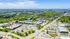 Vibrant aerial view of a bustling urban neighborhood with lush green spaces, modern apartments, and commercial buildings under a clear blue sky.