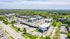 Aerial view of a vibrant residential complex surrounded by lush greenery, showcasing modern buildings and ample parking in a serene suburban setting.