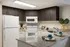 Modern kitchen with sleek granite countertops, stylish dark wood cabinets, and contemporary white appliances, including a refrigerator and microwave.