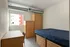 Contemporary bedroom with natural light, featuring a cozy bed, sleek desk, and ample storage in a modern apartment.