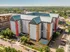 Impressive aerial view of a modern multi-story apartment complex with vibrant architectural design, lush surrounding greenery, and ample parking space.