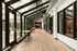 Modern apartment hallway with glass walls, wooden floors, and cozy seating looking out to a landscaped courtyard.