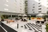 Modern courtyard featuring stylish seating, large umbrellas, greenery, and a life-sized checkers game against a sleek apartment backdrop.