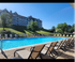 Bright, sunny poolside area with modern apartment buildings in the background, surrounded by lush greenery.