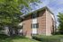 Brick building corner framed by leafy trees and hedges at Linden Colonial in Holladay, UT