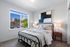 Bright and inviting bedroom with cozy bedding, modern artwork, and stunning city views from a large window.