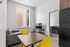 Modern apartment living space featuring a cozy sitting area with a sleek gray sofa, bright yellow chairs, and a flat-screen TV, seamlessly connected to a bedroom.