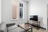 Modern apartment living room featuring sleek gray sofa, wooden coffee table, and a flat-screen TV, with large window offering ample natural light.