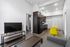 Modern living area with sleek kitchen, cozy gray sofa, vibrant yellow chairs, and a flat-screen TV offering stylish comfort.