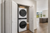 Modern apartment featuring a sleek in-unit laundry closet with a stacked washer and dryer, highlighting an abundance of natural light and a stylish open kitchen with plank floors.