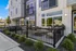 Modern apartment exterior with large glass windows, a stylish fenced patio, and lush landscaping.