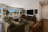 Inviting living room with plush green sectional, stylish wood furniture, and abundant natural light, offering a serene view of charming neighborhood homes.