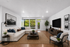 Modern living room with a plush beige sectional sofa, stylish decor, large windows offering lush views, and sleek wooden flooring.