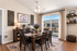 Elegant dining room with warm wood furniture, lavender centerpiece, and natural light through balcony doors in a cozy apartment setting.