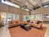 Clubhouse sitting area featuring two tan leather sofas and a grey stone coffee table all on top of a orange rug, surround by windows and doors for sunlight.