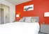 Queen size bed centered  against red  accent wall with two gray night stands with two lamps on each.