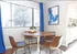 Brown dinning room table with four brown chairs, with blue curtains in the back ground, beautiful white kitchen sits in the distance