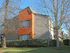 Building exterior with a orange accent pop out centered between two tall trees.