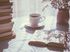 A table topped with an open book, a cup of coffee and a plant, with gentle light streaming in through a window.