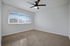 White walls, brown carpet, brown ceiling fan with wide window on left back wall