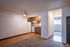 cool toned living room with a view into the kitchen and hallway, with white walls, vinyl flooring and dark baseboards and black accents